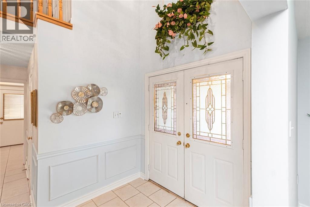 Entryway featuring double doors with decorative glass inserts, ceramic tile flooring, wainscoting, and a wooden staircase with balusters - 85 Citation Crescent, Ancaster, ON
