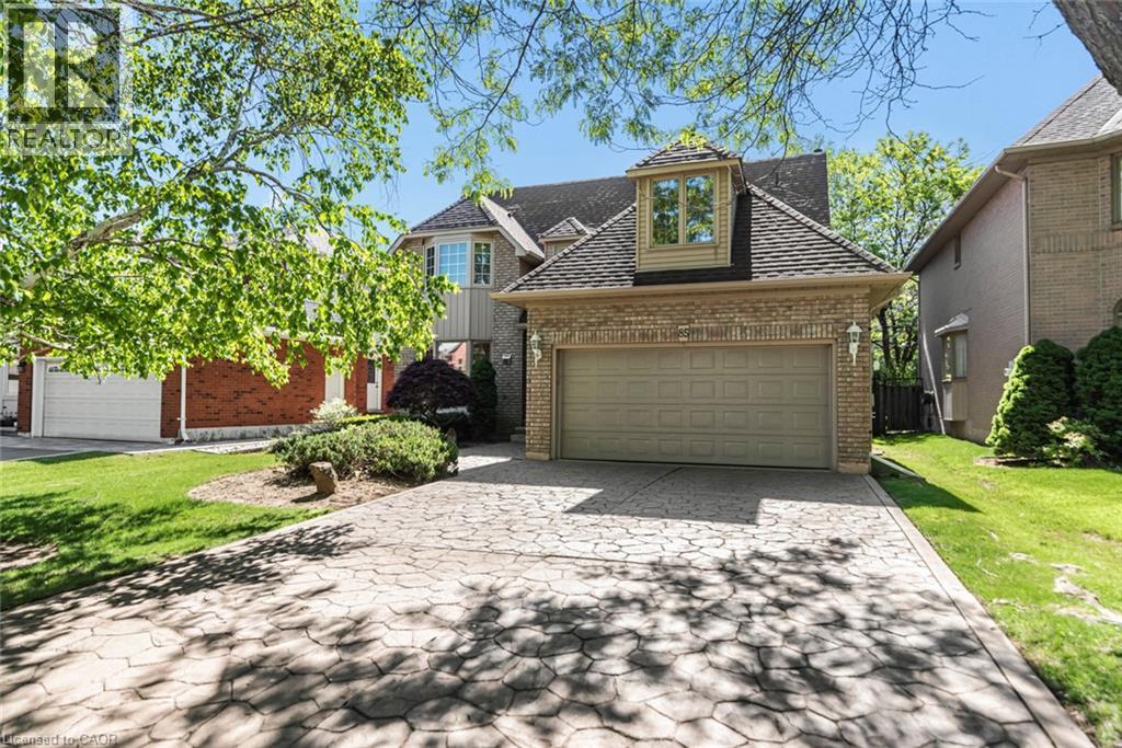 Brick exterior with a prominent two-car garage, featuring a stamped concrete driveway, dormer window, and mature front landscaping - 85 Citation Crescent, Ancaster, ON