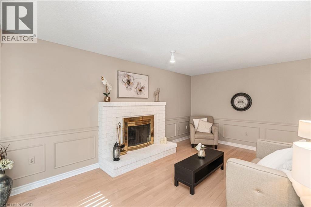 Living area featuring a white brick fireplace with a brass firebox, wainscoting, light wood-finish flooring, and recessed lighting - 85 Citation Crescent, Ancaster, ON