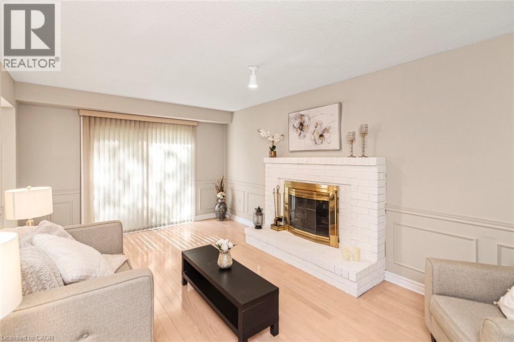 Living area featuring a white brick fireplace with a brass insert, light wood-finish flooring, wainscoting, and sliding glass doors - 85 Citation Crescent, Ancaster, ON