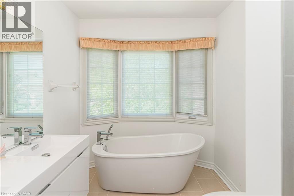 Freestanding soaking tub with chrome hardware, set against a bay window with natural light - 85 Citation Crescent, Ancaster, ON