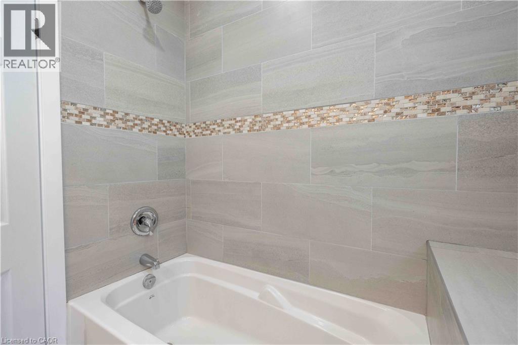 Bathtub and shower combination featuring large format grey wall tiles, a decorative mosaic tile accent band, and a chrome shower head and faucet - 204 Glow Avenue Unit# Upper, Hamilton, ON