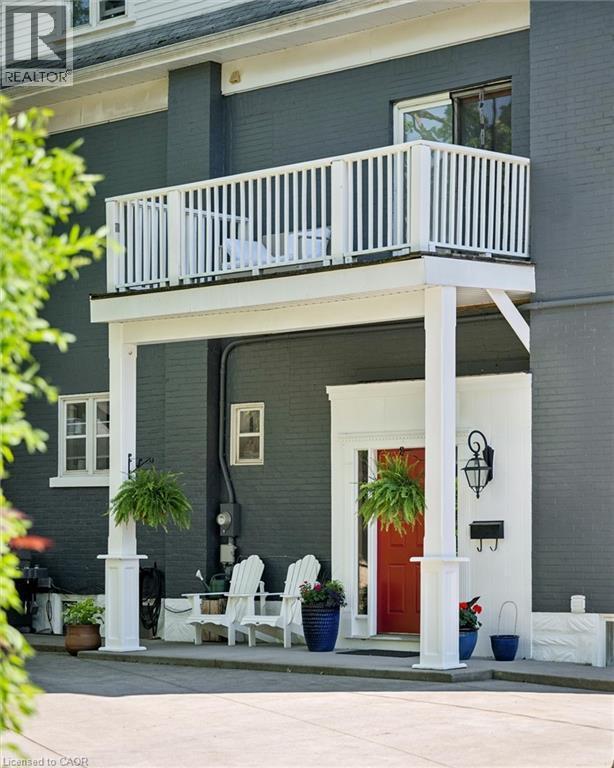 Exterior featuring a second-story balcony with white railings, a covered patio below, a prominent red entry door, an exterior wall lantern, and dark-painted brick siding - 149 Young Street, Kitchener, ON - Outdoor