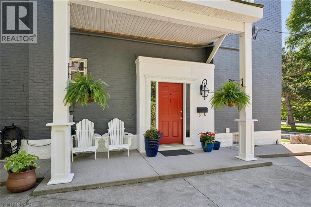 Covered porch entry featuring a vibrant red door, a black exterior lantern, and dark gray brick siding - 149 Young Street, Kitchener, ON - Outdoor