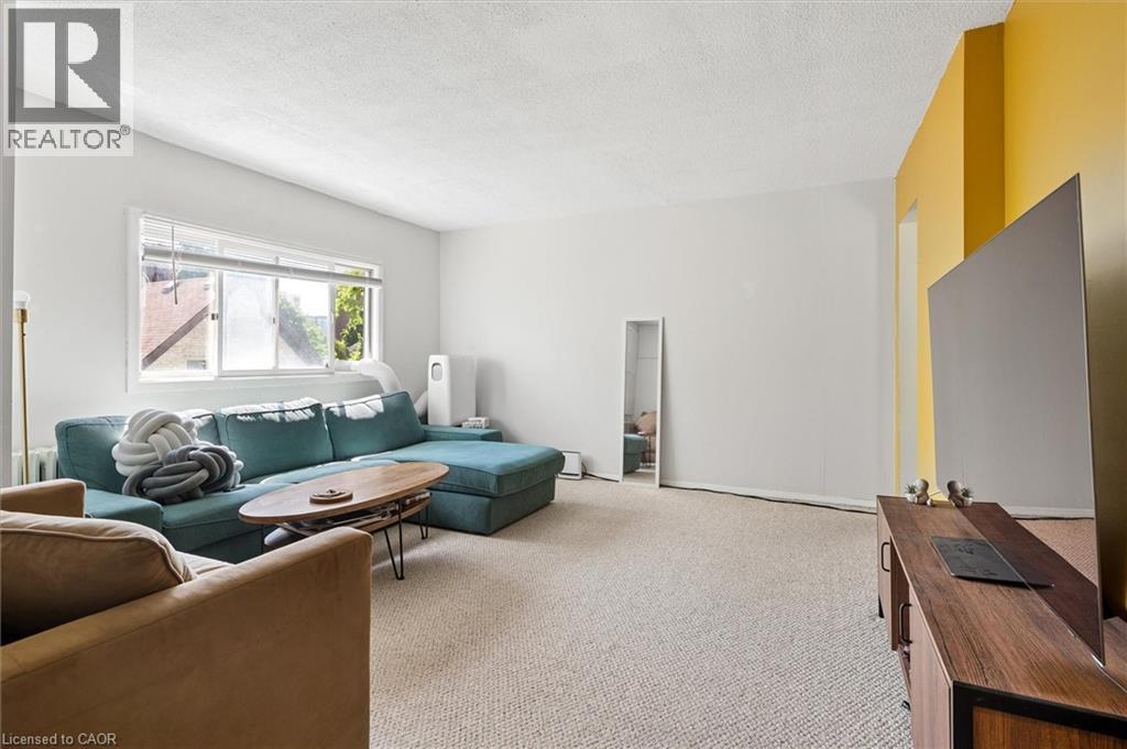 Carpeted living area featuring a large window, white walls, and an accent wall with a bright yellow finish - 149 Young Street, Kitchener, ON - Indoor Photo Showing Living Room