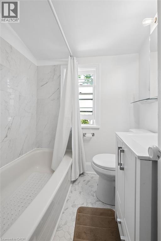 Bathroom featuring a built-in tub with tile surround, white hex tile flooring, white vanity with integrated sink, and an integrated wall mirror with shelf - 149 Young Street, Kitchener, ON - Indoor Photo Showing Bathroom