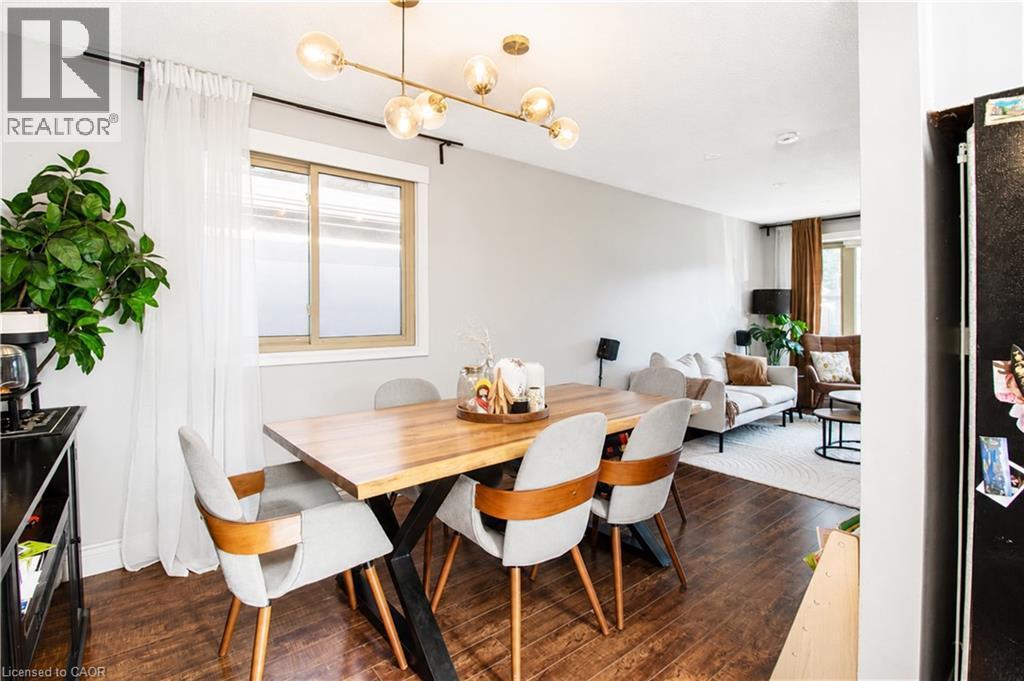 Dining area featuring wood-finish flooring, a contemporary linear chandelier, and a large window with white sheer curtains - 103 Mcanulty Boulevard Unit# Upper, Hamilton, ON