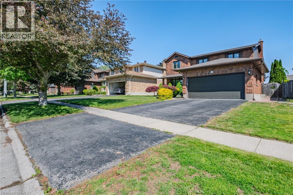 Brick two-story residence featuring a dark garage door, paved driveway, mature front yard trees, and perimeter fencing - 141 Lynndale Road, Simcoe, ON