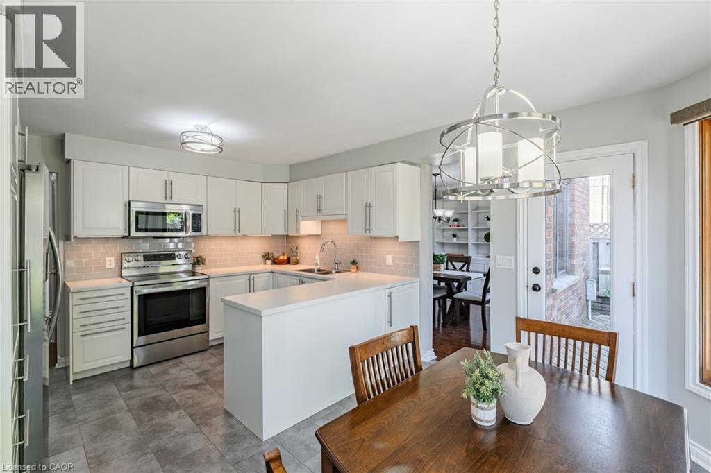 Kitchen featuring white cabinetry, stainless steel appliances, a light-toned tile backsplash, and a contemporary pendant light fixture - 141 Lynndale Road, Simcoe, ON