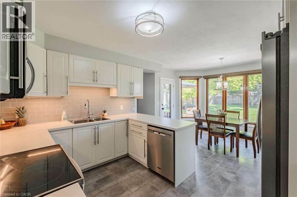 Kitchen featuring white shaker cabinetry, stainless steel appliances, light subway tile backsplash, and a double basin sink - 141 Lynndale Road, Simcoe, ON