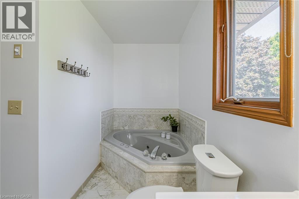 Corner jetted tub with tiled surround, wood-framed window, and white commode - 141 Lynndale Road, Simcoe, ON
