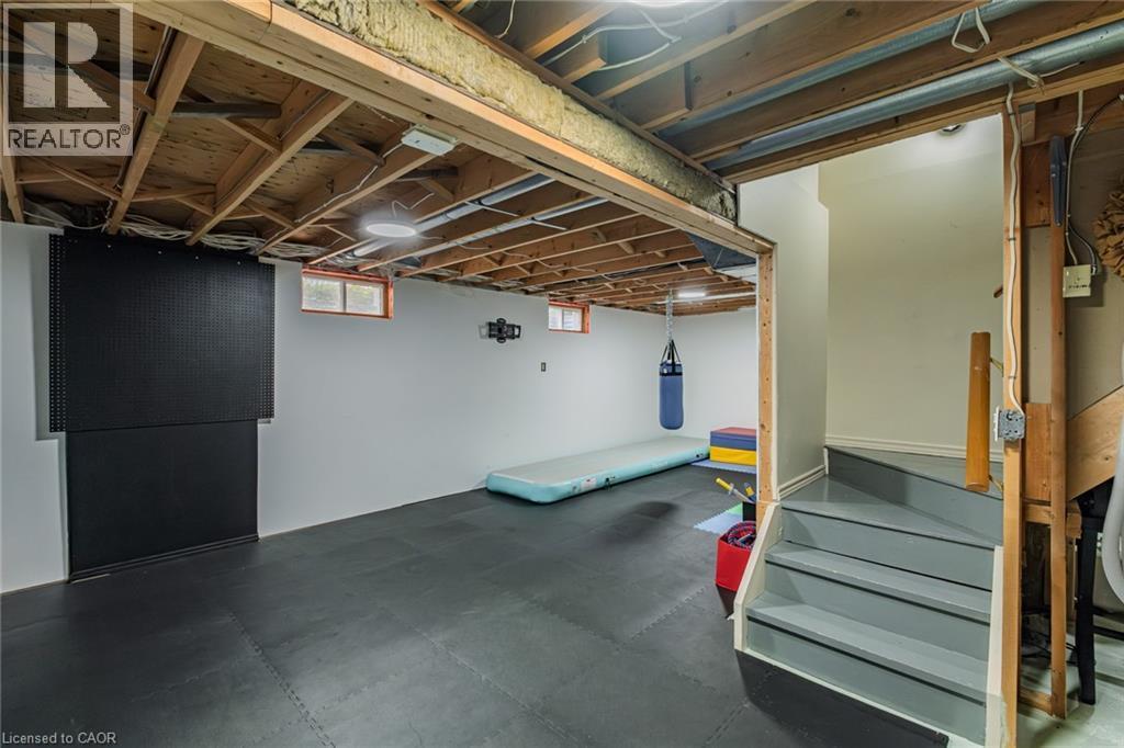 Finished basement area featuring resilient black flooring, exposed ceiling joists, and painted white walls - 141 Lynndale Road, Simcoe, ON