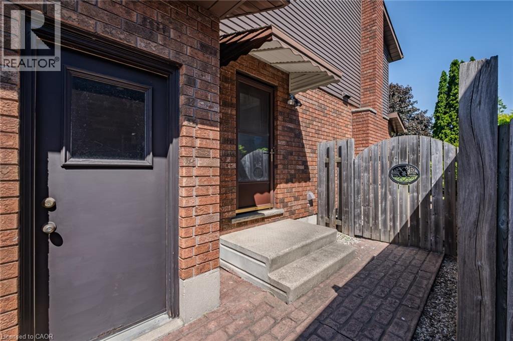 Brick exterior featuring a black door with upper window pane, concrete steps, and a wooden privacy fence with gate - 141 Lynndale Road, Simcoe, ON