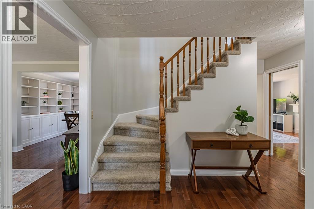 Carpeted staircase with wooden banister, dark wood-finish flooring, white built-in shelving with lower cabinetry, and light gray wall paint - 141 Lynndale Road, Simcoe, ON