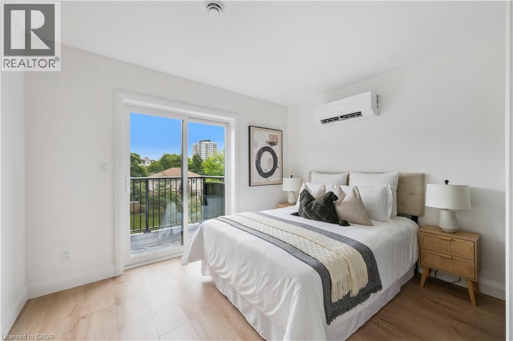Bedroom featuring light wood-finish flooring, white walls, and a sliding glass door leading to a balcony with black metal railings - 60 Arlington Boulevard Unit# 3, Kitchener, ON