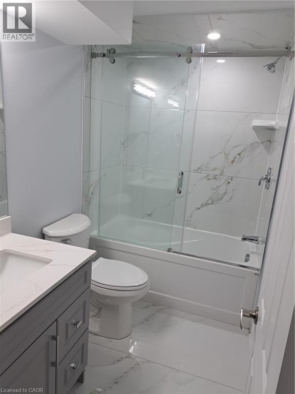 Bathroom featuring a white bathtub with a sliding glass door enclosure, a single vanity with a gray wood-finish cabinet, and a white countertop - 2240 Headon Road Unit# Lower, Burlington, ON