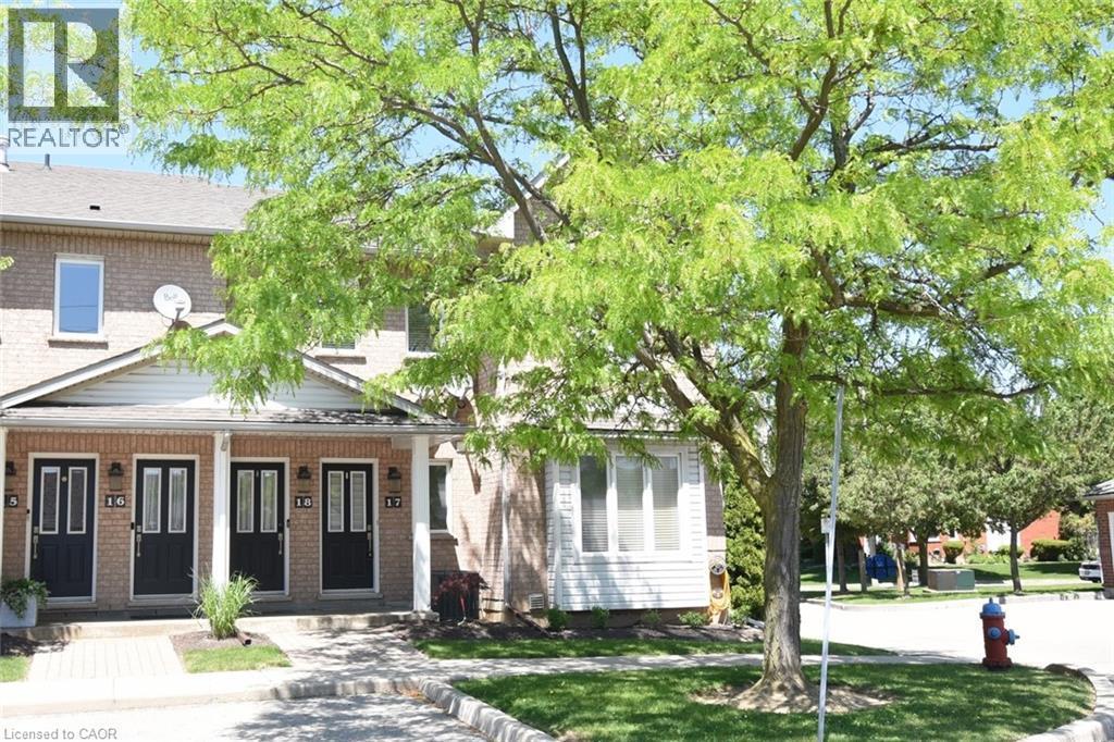 Brick facade townhome featuring black paneled front doors with glass inserts, covered entry porches, white gabled accents, and a mature shade tree - 2 Harbour Drive Unit# 17, Stoney Creek, ON