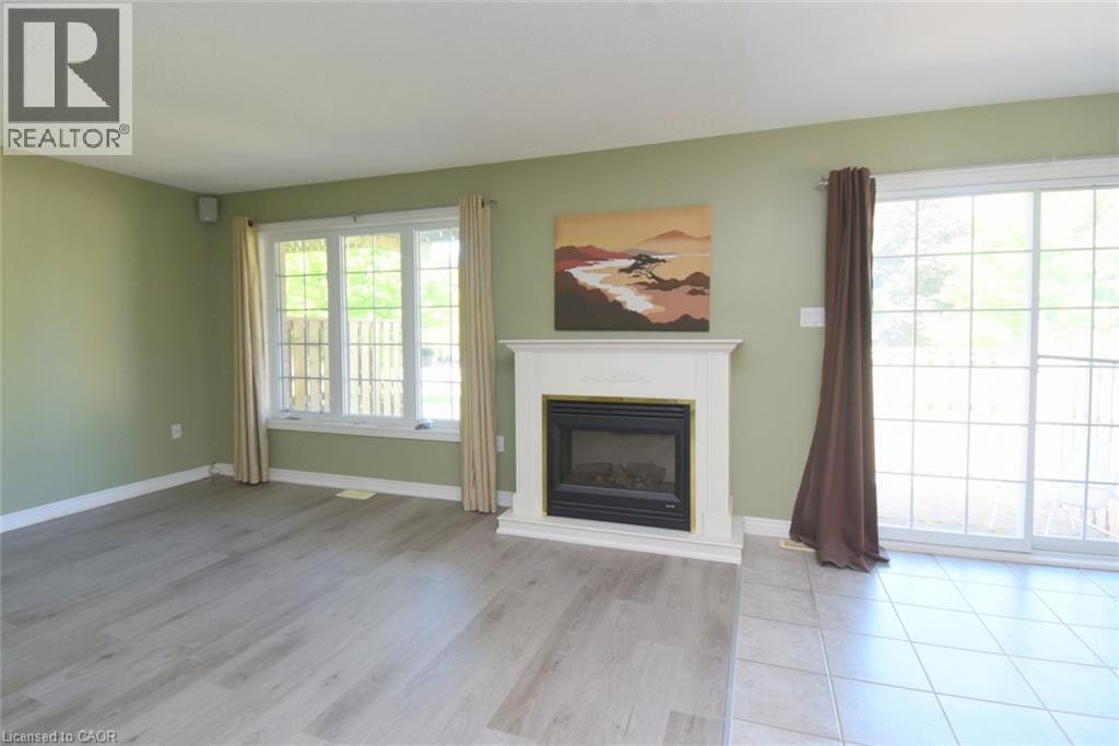 Living area featuring a white fireplace with a black and brass insert, wood-finish flooring, a bay window, and a sliding glass door - 2 Harbour Drive Unit# 17, Stoney Creek, ON