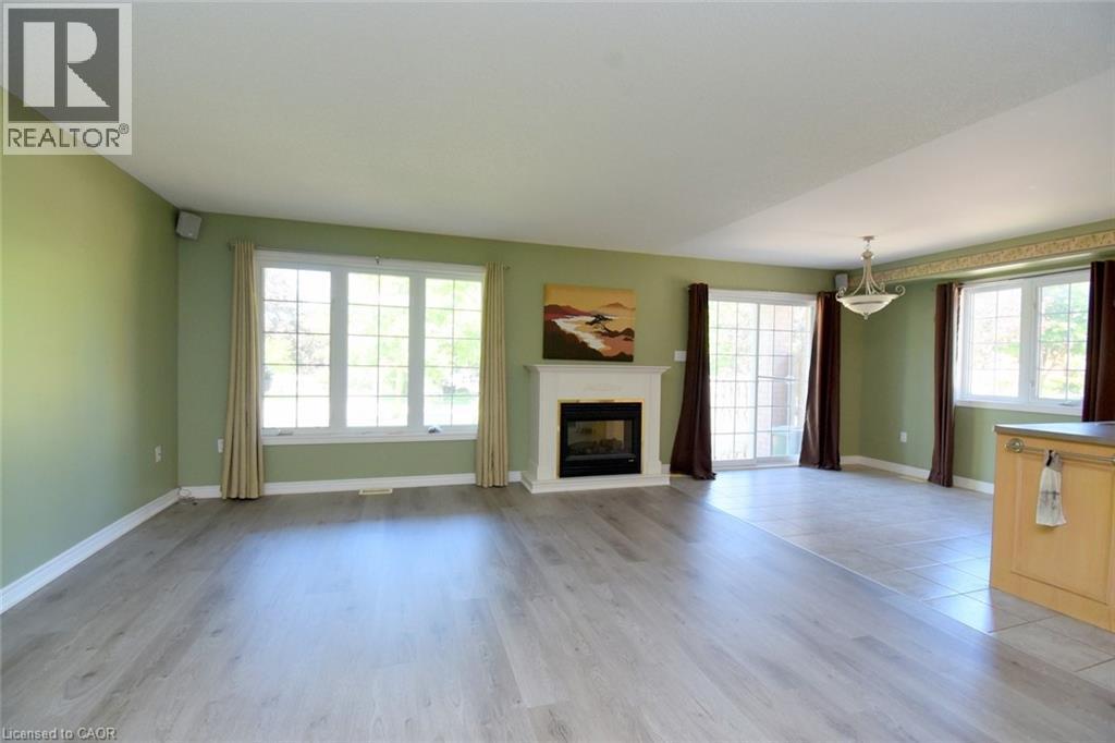 Spacious room featuring light wood-finish flooring, a white mantel fireplace, and multiple large windows - 2 Harbour Drive Unit# 17, Stoney Creek, ON
