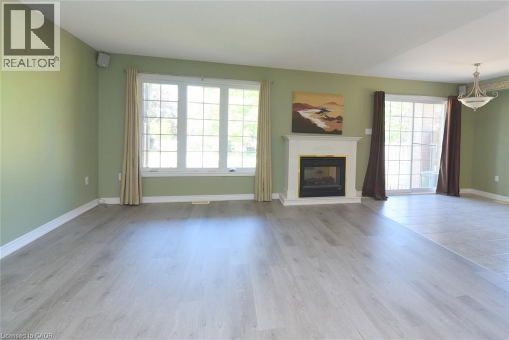 Living area featuring a fireplace with a white mantel, wood-finish flooring, and a large window - 2 Harbour Drive Unit# 17, Stoney Creek, ON