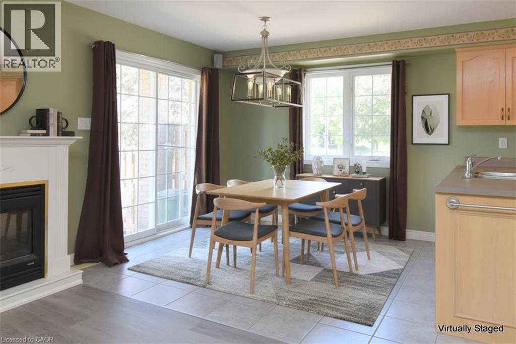 Dining area featuring a contemporary linear chandelier, a white mantel with an electric fireplace, and a large sliding glass door - 2 Harbour Drive Unit# 17, Stoney Creek, ON