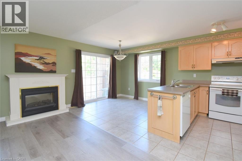 Open-concept living space featuring a white fireplace with a black insert, wood-finish flooring, and a sliding glass door - 2 Harbour Drive Unit# 17, Stoney Creek, ON