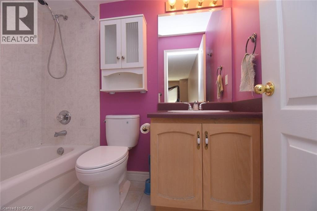 Full bathroom featuring a white bathtub with a tiled surround, a toilet, and a light wood-finish vanity with a built-in sink and an overhead mirrored medicine cabinet - 2 Harbour Drive Unit# 17, Stoney Creek, ON