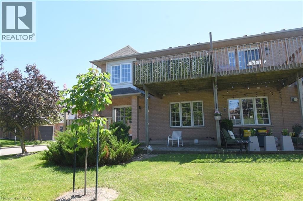 Expansive lawn area featuring a multi-level brick exterior, a ground-level patio, and an upper-level wooden deck with balusters - 2 Harbour Drive Unit# 17, Stoney Creek, ON
