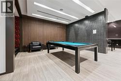 Recreational room featuring a billiards table with turquoise felt, wood-finish flooring, accent wall with dark brick-patterned tile, and recessed linear ceiling lighting -