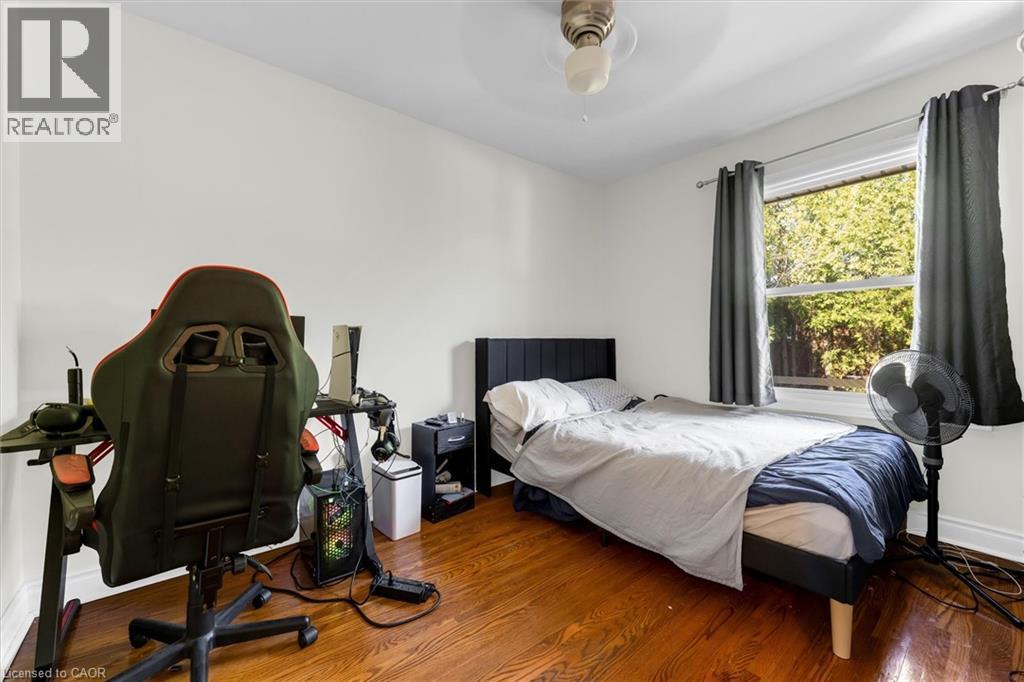 Hardwood-finish flooring featuring a window with exterior views, a ceiling fan, and white painted walls - 406 East 43Rd Street, Hamilton, ON