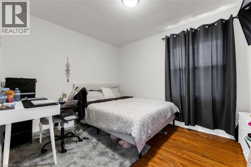 Bedroom featuring hardwood flooring, white painted walls, and a window with dark curtains - 406 East 43Rd Street, Hamilton, ON