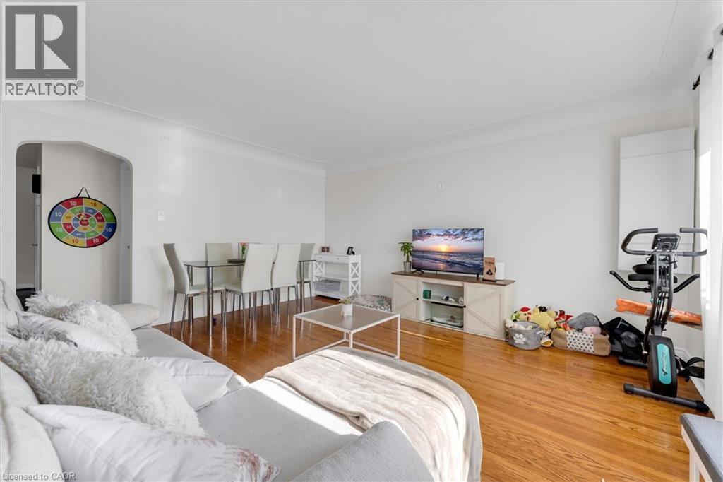 Hardwood-finish flooring spans this open-concept room, featuring bright white walls and an arched doorway - 406 East 43Rd Street, Hamilton, ON
