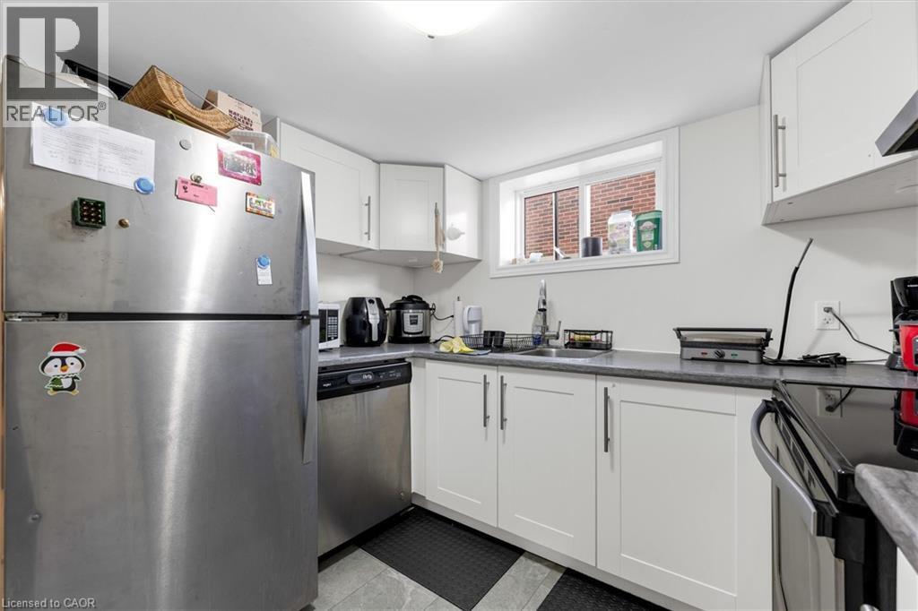 Kitchen featuring white cabinetry, gray countertops, stainless steel appliances, and a window with a brick exterior visible - 406 East 43Rd Street, Hamilton, ON