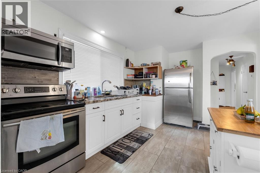 Kitchen featuring stainless steel appliances, white cabinetry, granite-finish countertops, tile flooring, and an arched doorway - 406 East 43Rd Street, Hamilton, ON