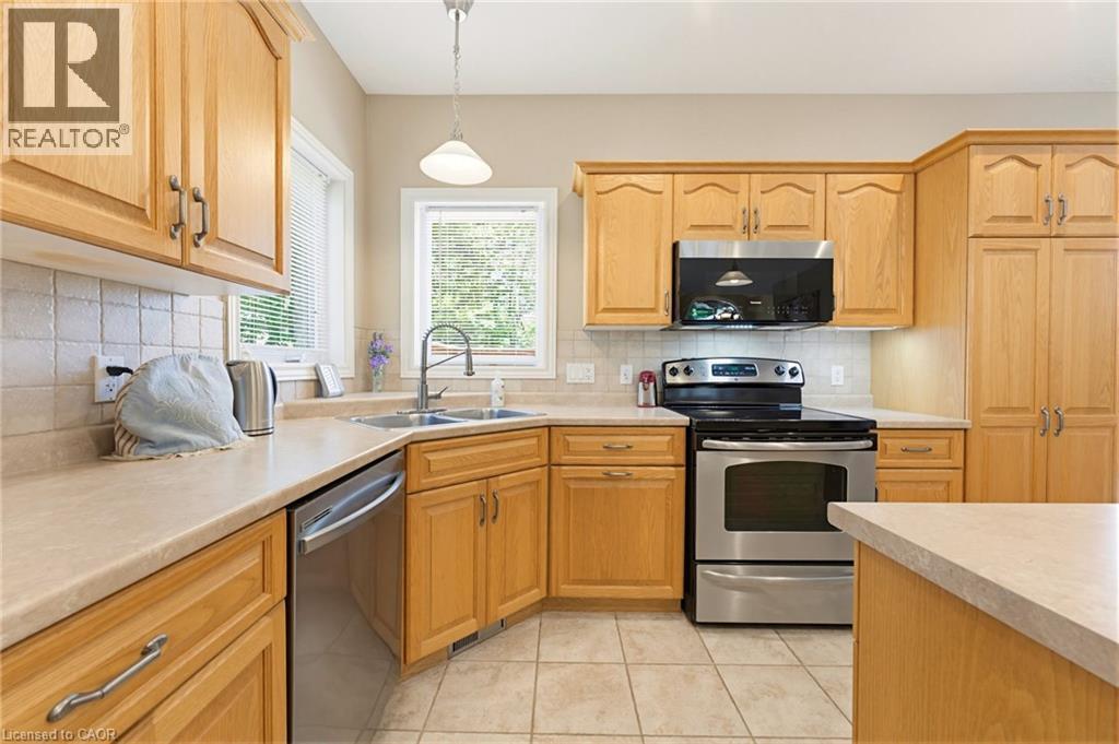 Kitchen featuring light wood cabinetry, a corner sink with a window, stainless steel appliances, and tile flooring - 5 Coastal Court, Port Dover, ON