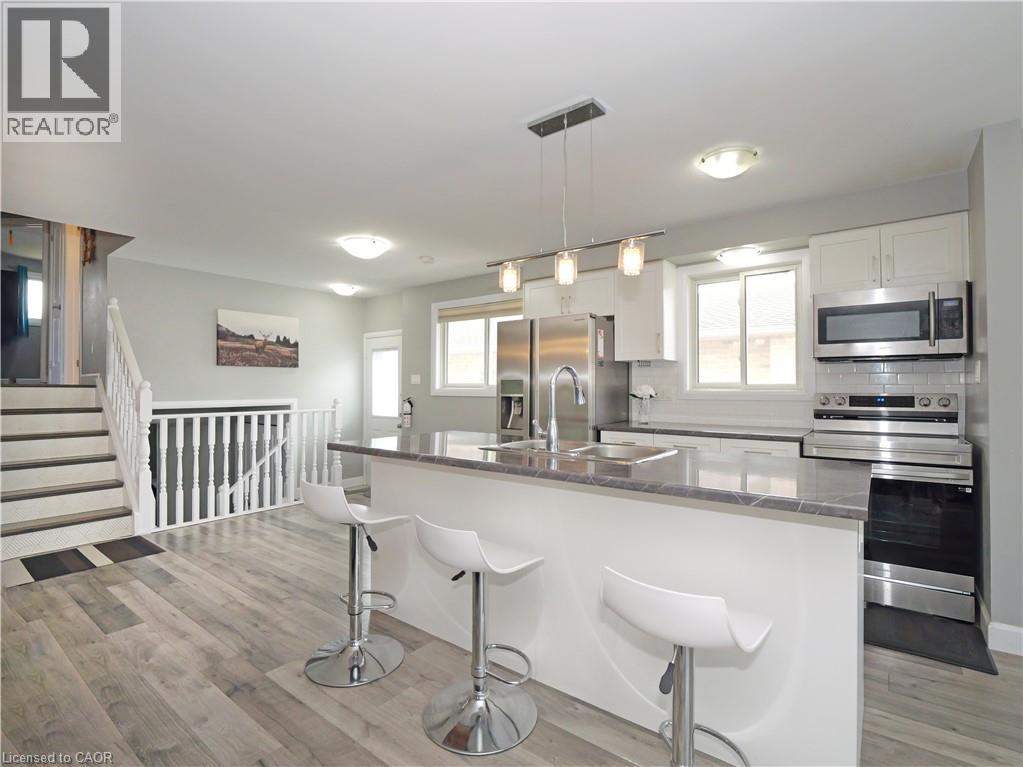 Open-concept kitchen featuring an island with stone-finish countertop, stainless steel appliances, white cabinetry, and wood-finish flooring - 771 Monsarrat Avenue, London, ON