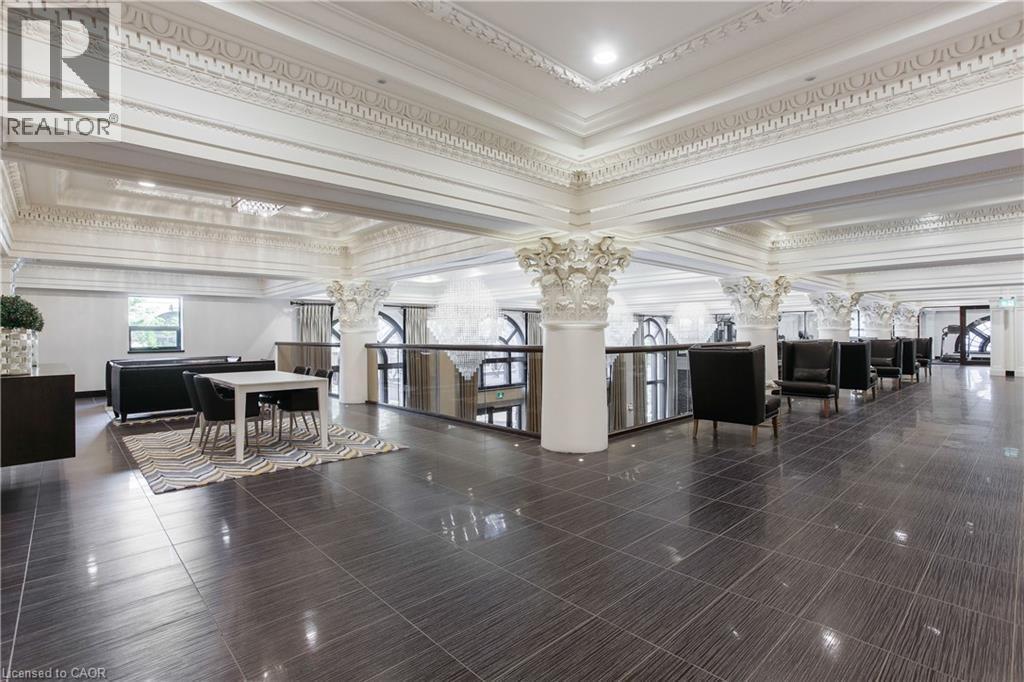 Expansive interior space featuring dark large-format tile flooring, ornate ceiling molding, decorative columns, and a glass-paneled railing system - 112 King Street E Unit# Ph6, Hamilton, ON - Indoor Photo Showing Other Room