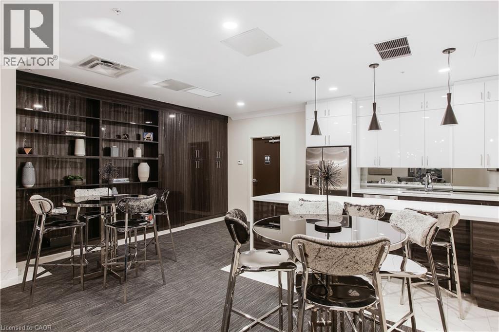 Contemporary kitchen and lounge area featuring dark wood-finish built-in shelving, white high-gloss cabinetry, a stainless steel refrigerator, and pendant lighting fixtures - 112 King Street E Unit# Ph6, Hamilton, ON - Indoor Photo Showing Dining Room