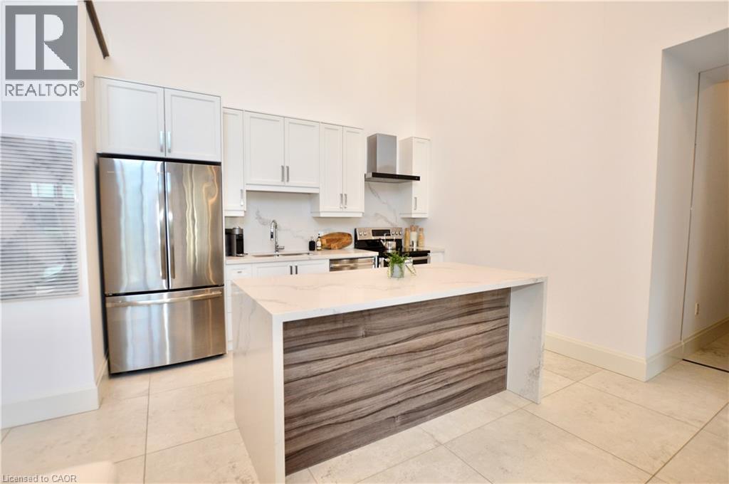 Modern kitchen featuring white cabinetry, stainless steel appliances, and a waterfall-edge island with wood-finish paneling - 112 King Street E Unit# Ph6, Hamilton, ON - Indoor Photo Showing Kitchen With Stainless Steel Kitchen