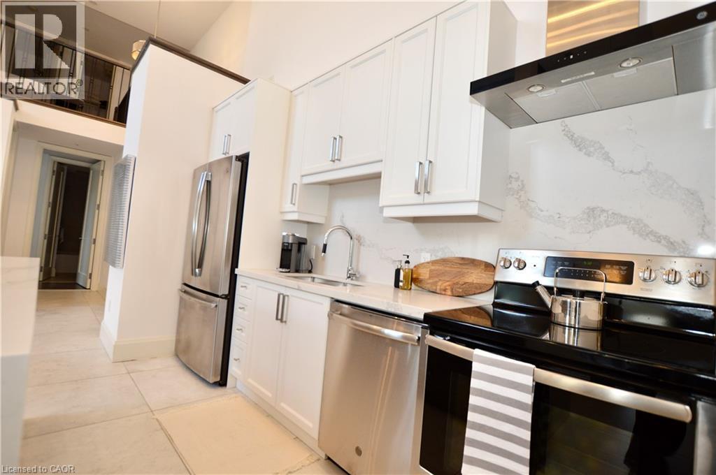 Modern kitchen featuring white cabinetry, stainless steel appliances, a white patterned backsplash, a stainless steel range hood, and light-toned tile flooring - 112 King Street E Unit# Ph6, Hamilton, ON - Indoor Photo Showing Kitchen With Stainless Steel Kitchen