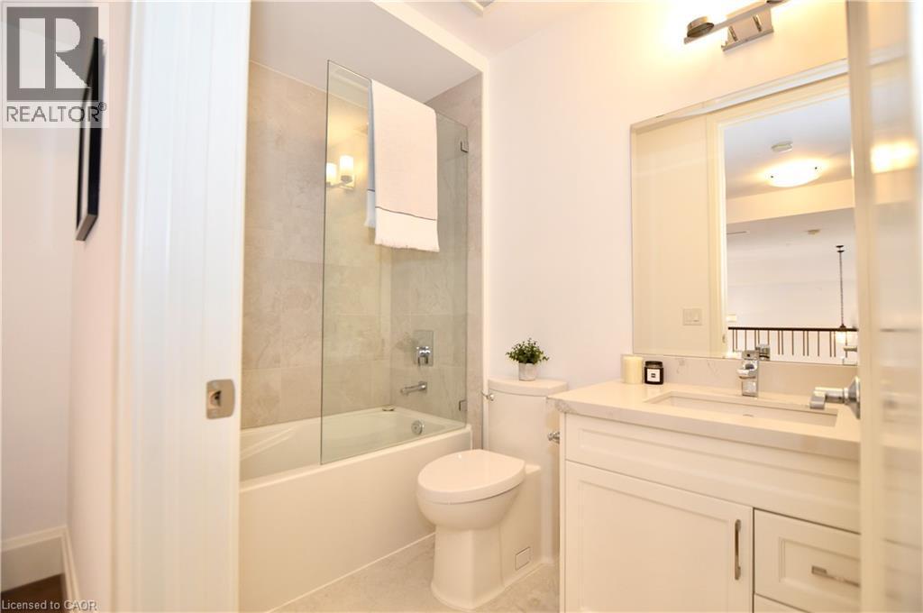 Full bathroom featuring a white vanity with integrated sink, a built-in tub with a clear glass enclosure, and a tile shower surround - 112 King Street E Unit# Ph6, Hamilton, ON - Indoor Photo Showing Bathroom