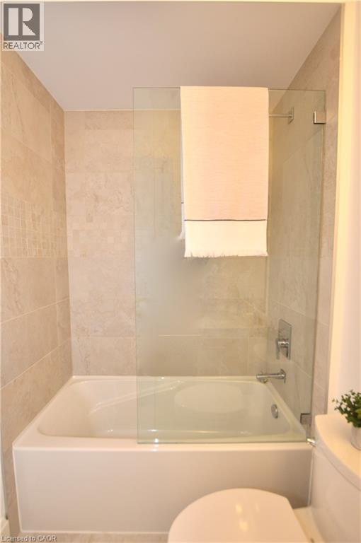 Bathtub with a partial glass shower screen, chrome fixtures, and neutral tile surround extending to the ceiling - 112 King Street E Unit# Ph6, Hamilton, ON - Indoor Photo Showing Bathroom
