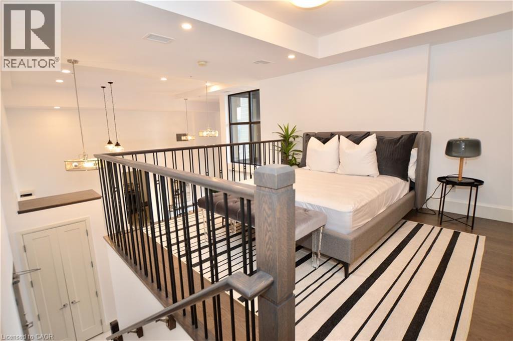 Open-concept loft space featuring a dark wood-finish flooring and a contemporary black metal and wood-tone railing system - 112 King Street E Unit# Ph6, Hamilton, ON - Indoor Photo Showing Other Room