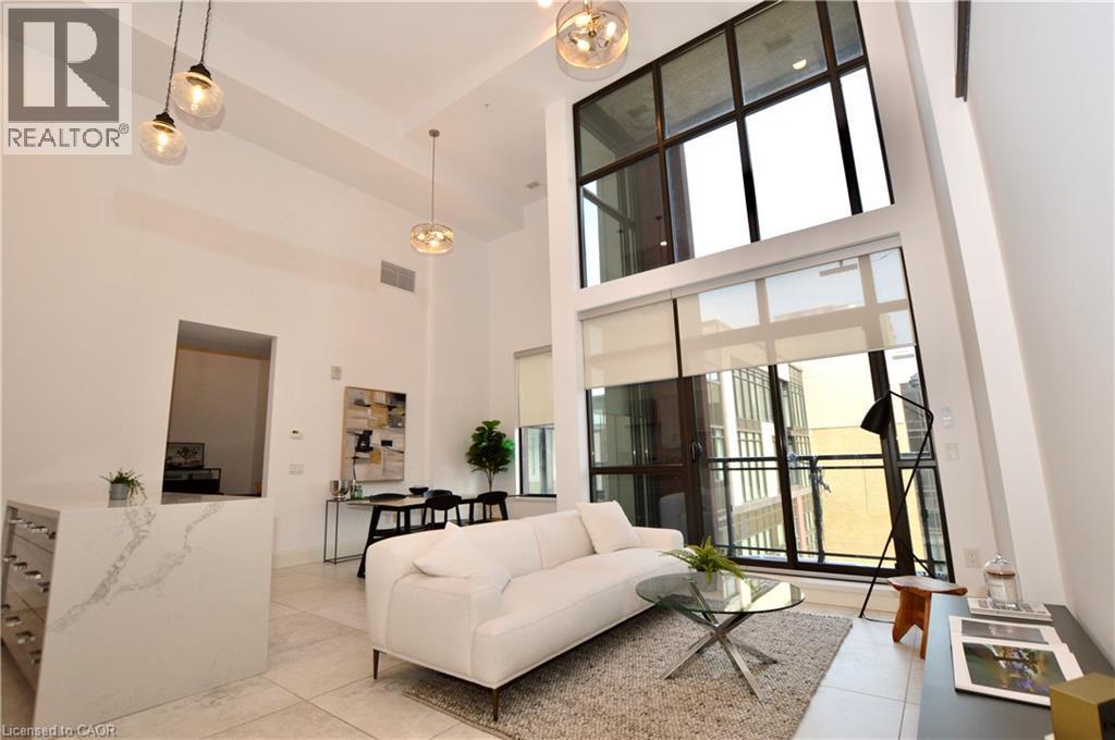 Two-story window wall with roller shades, high ceilings with pendant lighting, a kitchen island with a waterfall countertop and integrated wine storage, and light-toned tile flooring - 112 King Street E Unit# Ph6, Hamilton, ON - Indoor