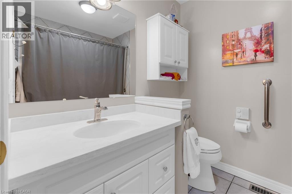 Bathroom featuring a white vanity with an integrated sink, brushed nickel faucet, wall-mounted mirror, white wall cabinetry, and tile flooring - 50 Spadara Drive, Hamilton, ON