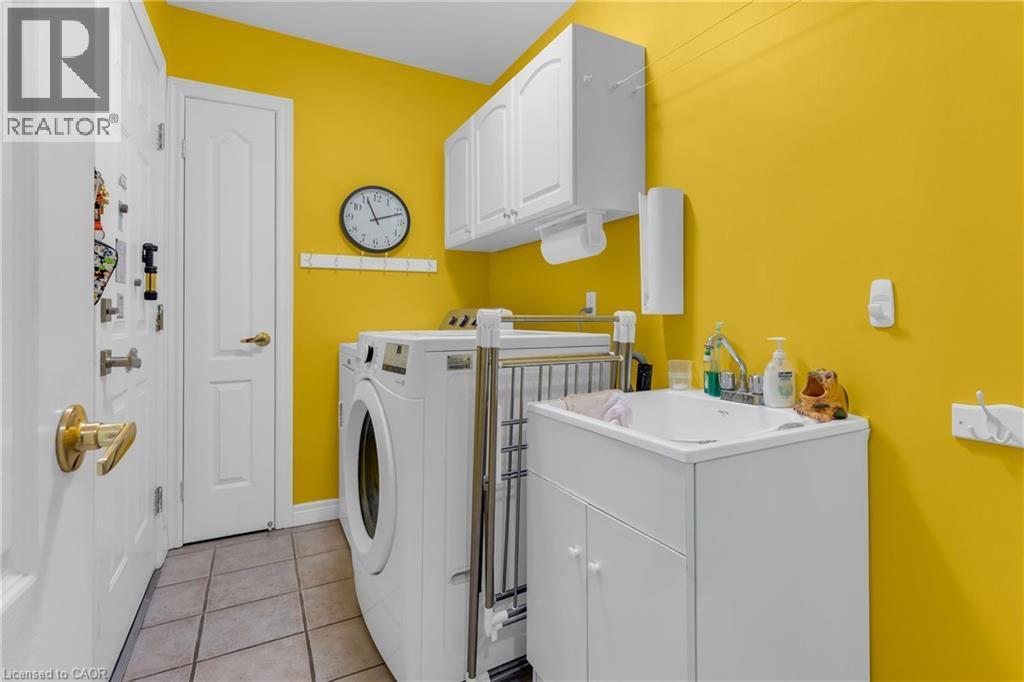 Laundry area featuring tile flooring, white cabinetry, a utility sink with a built-in cabinet, and a wall-mounted paper towel dispenser - 50 Spadara Drive, Hamilton, ON