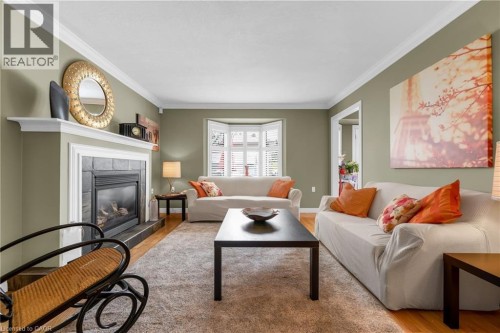 Spacious room featuring a fireplace with a slate surround and mantle, hardwood flooring, bay window with plantation shutters, and crown molding - 50 Spadara Drive, Hamilton, ON - Indoor Photo Showing Living Room With Fireplace