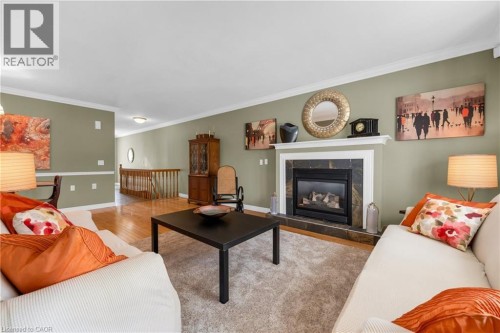 Living space featuring a fireplace with a white mantel and dark tile surround, hardwood flooring, soft green walls, and white crown molding - 50 Spadara Drive, Hamilton, ON - Indoor Photo Showing Living Room With Fireplace