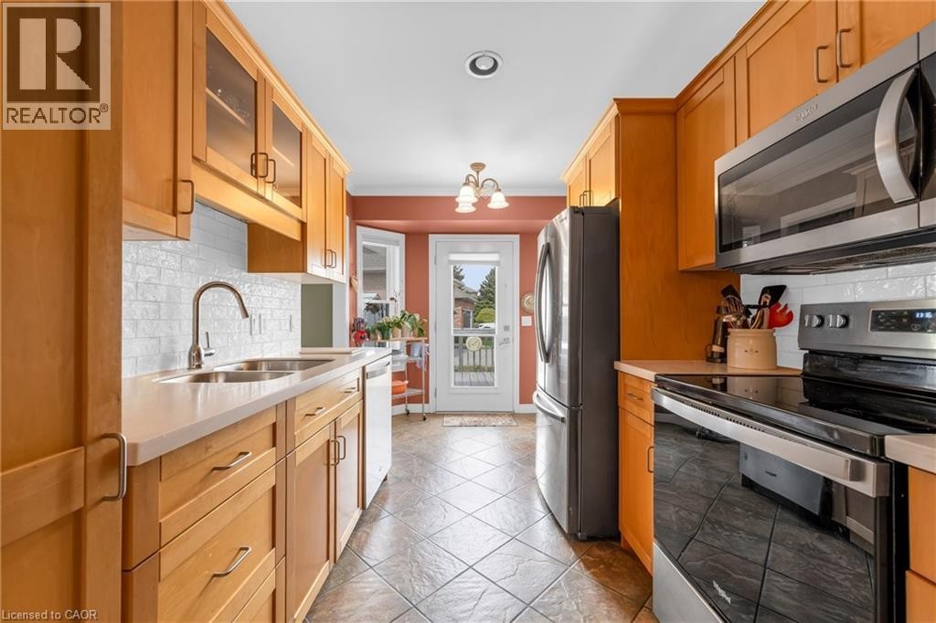 Galley kitchen featuring light wood cabinetry, stainless steel appliances, a double basin sink, white subway tile backsplash, and light-toned countertops - 50 Spadara Drive, Hamilton, ON - Indoor Photo Showing Kitchen With Double Sink
