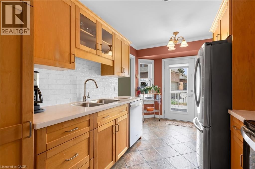 Kitchen featuring wood cabinetry, light-toned countertops, a white subway tile backsplash, a stainless steel double basin sink with a gooseneck faucet, and ceramic tile flooring - 50 Spadara Drive, Hamilton, ON - Indoor Photo Showing Kitchen With Double Sink